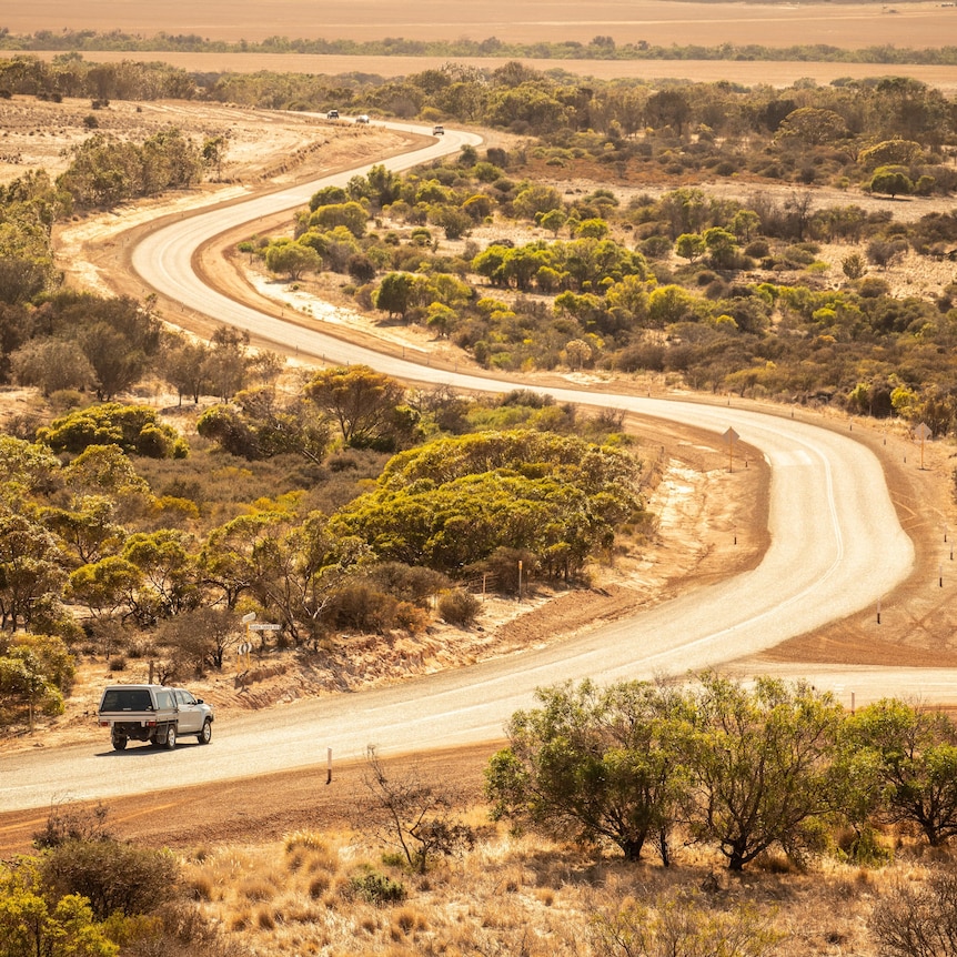 Ultra wide shot of a ute driving down a country road in iconic red-dirt Australian outback.