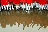 A group of girls wearing red skirts and long white socks shown from the waist down are reflected in a big puddle