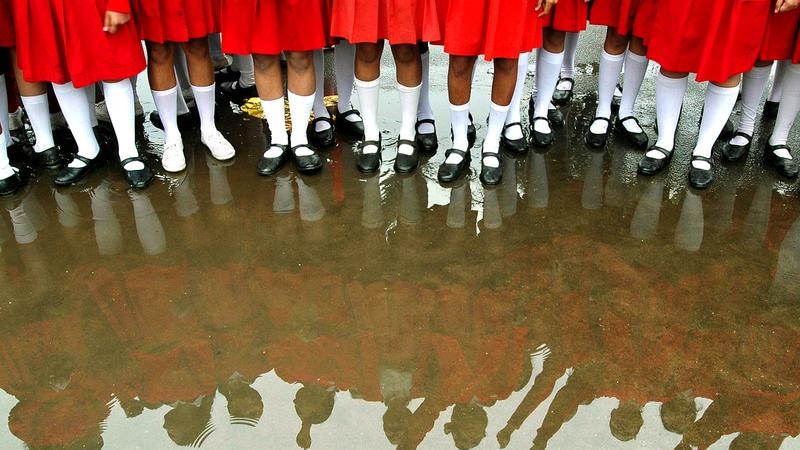 A group of girls wearing red skirts and long white socks shown from the waist down are reflected in a big puddle