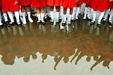 A group of girls wearing red skirts and long white socks shown from the waist down are reflected in a big puddle