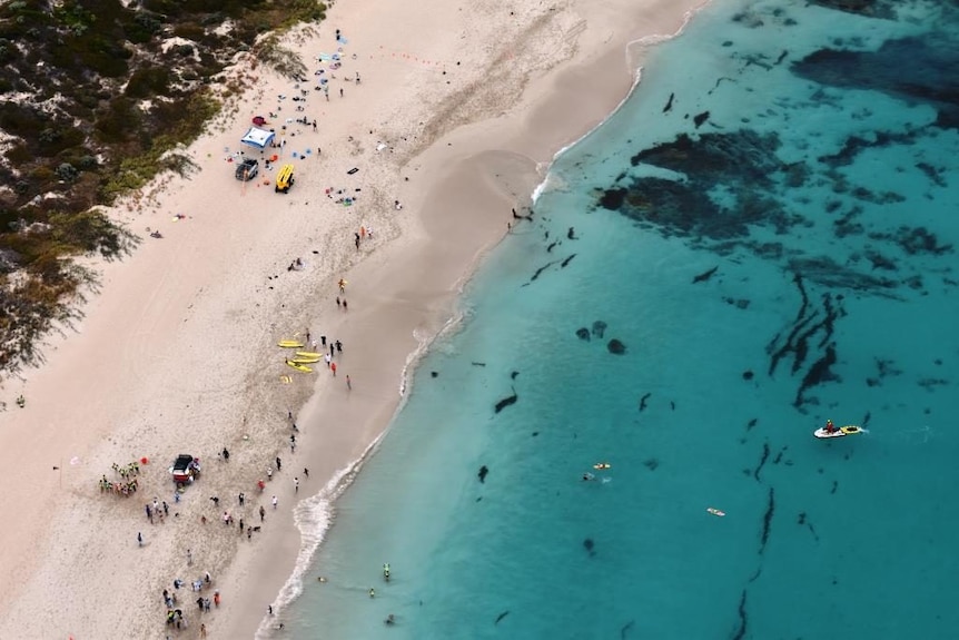 An overhead show of a beach with white sand, blue water and people on it.