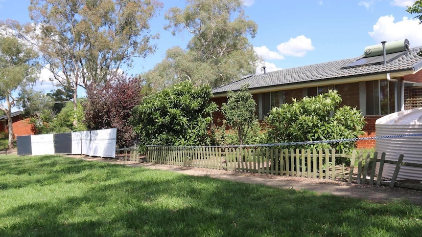 Australian Federal Police barrier can be seen outside the house, also trees lined up along fence.