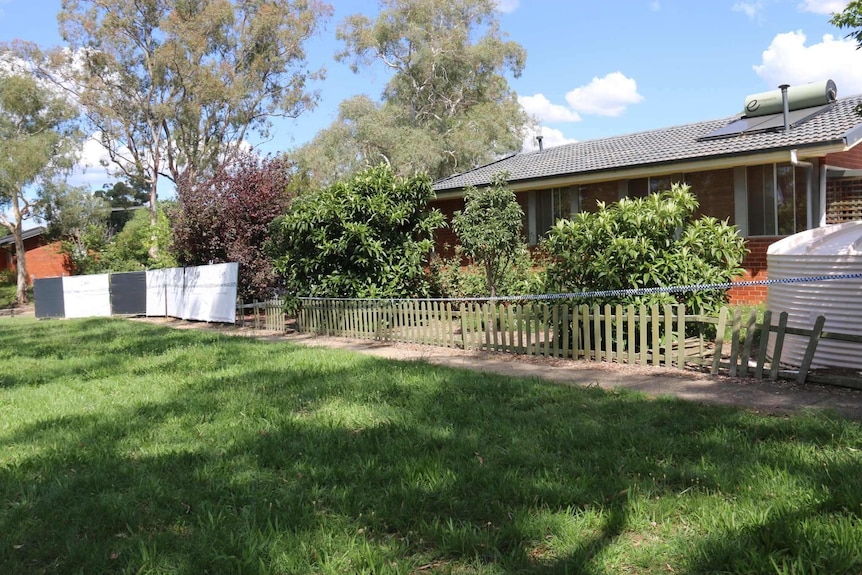 Australian Federal Police barrier can be seen outside the house, also trees lined up along fence.