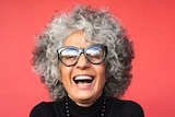 A woman with curly grey hair smiles against a red backdrop.