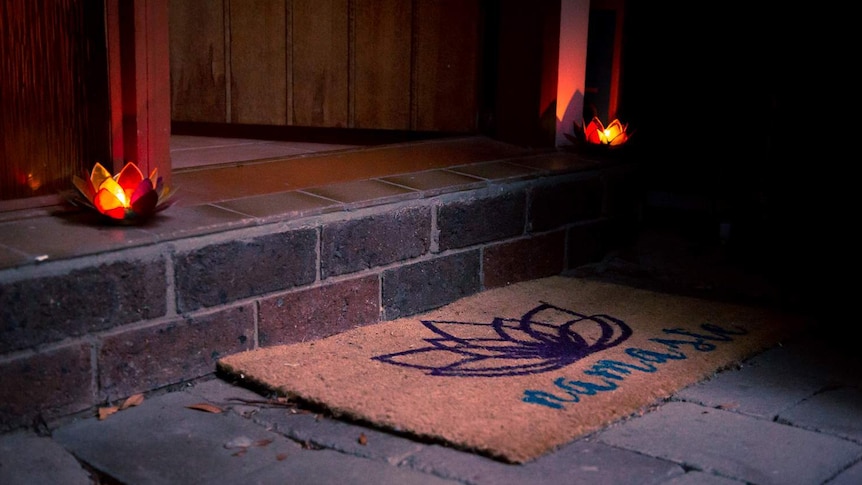 A welcome mat reading Namaste is at an open door, with two candles lit on either side.