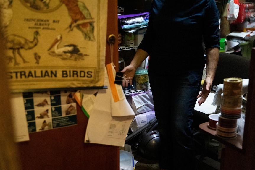 A woman looks surprised as she opens a cupboard stacked to the brim with food.