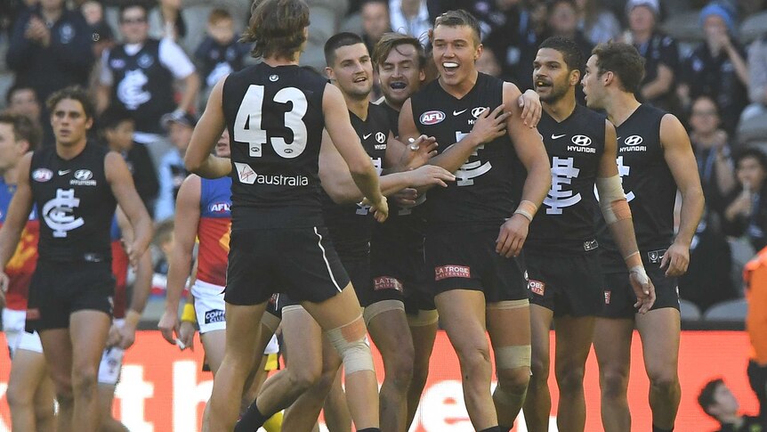 A number of Carlton players surround Patrick Cripps, who smiles while being hugged.