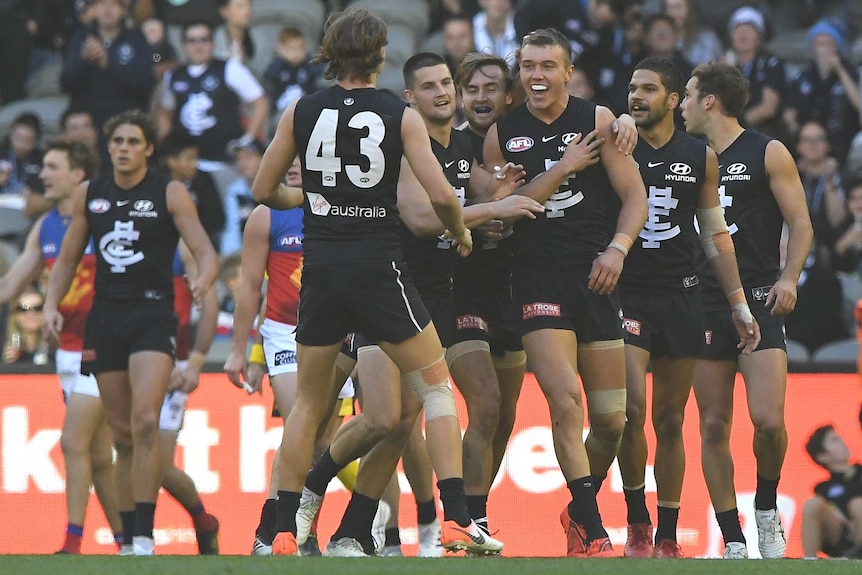 A number of Carlton players surround Patrick Cripps, who smiles while being hugged.