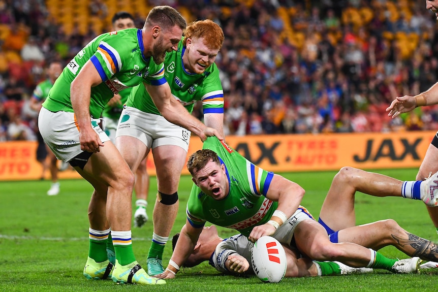 A group of Canberra NRL players grab their teammate by the jumper to lift him up after scoring a try.