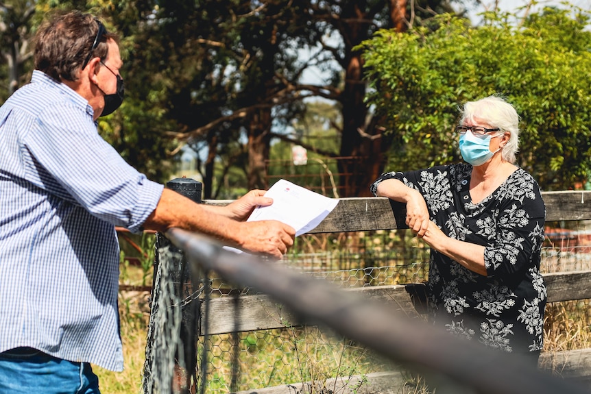 A man and a woman wearing masks speak over a fence