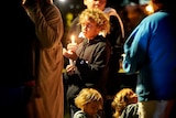 A boy with light curly hair holds a candle at a vigil