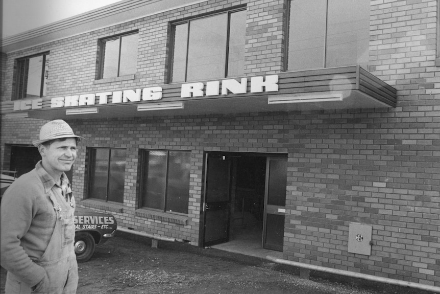 Black and white image of a man in overalls outside a brick building in the 1980s