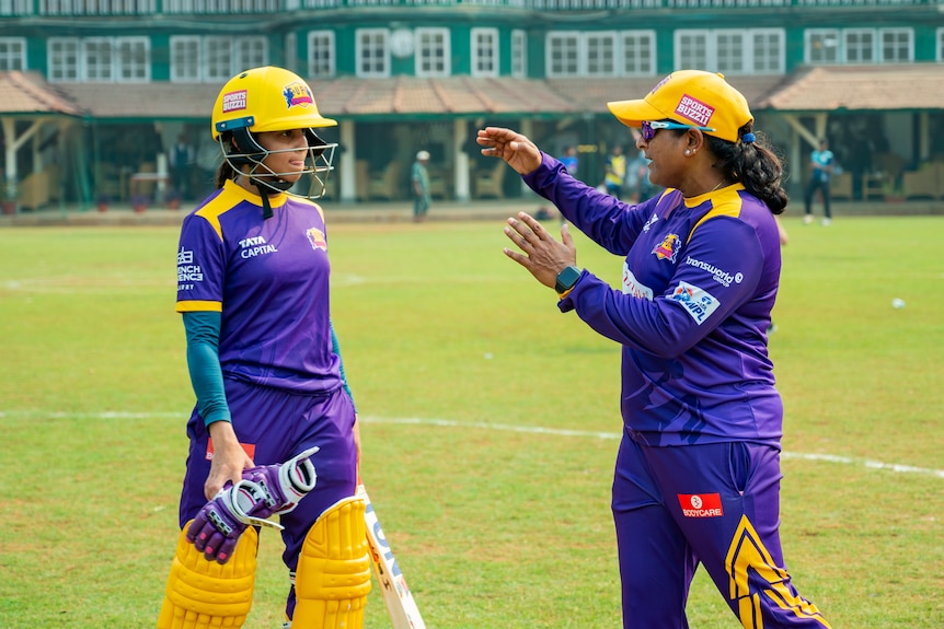 Anju Jain speaks to a player on the cricket field.