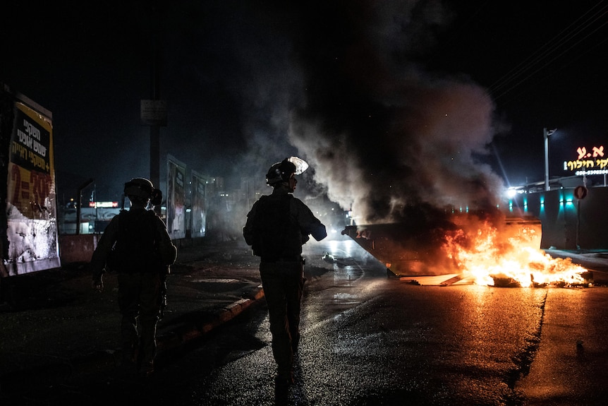 The silhouette of a police officer is seen against a backdrop of fire. 