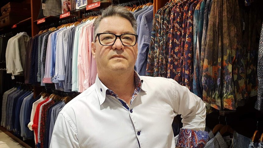 Jamie Warner, owner of Studio 196 in Chermside, poses in front of men's dress shirts.