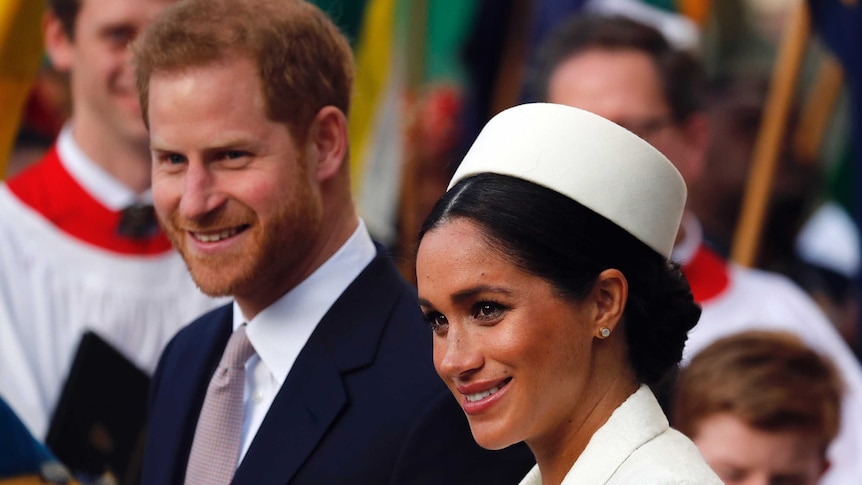 A woman in a white hat and a man in a suit smile