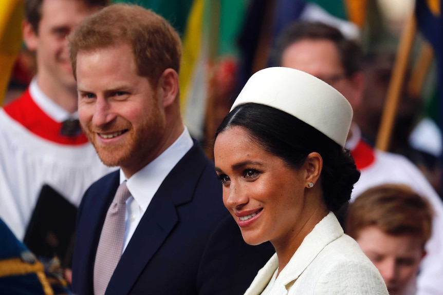 A woman in a white hat and a man in a suit smile