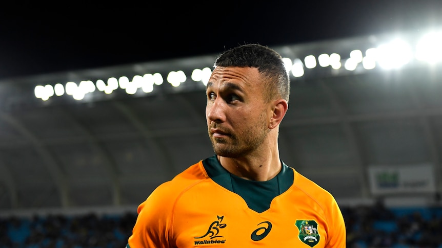 Quade Cooper looks over his right shoulder in a stadium wearing a gold Wallabies jersey