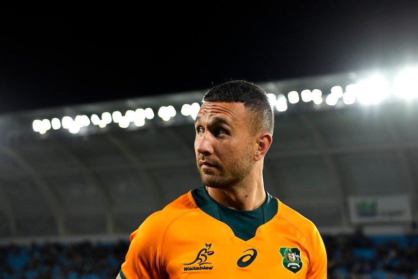 Quade Cooper looks over his right shoulder in a stadium wearing a gold Wallabies jersey