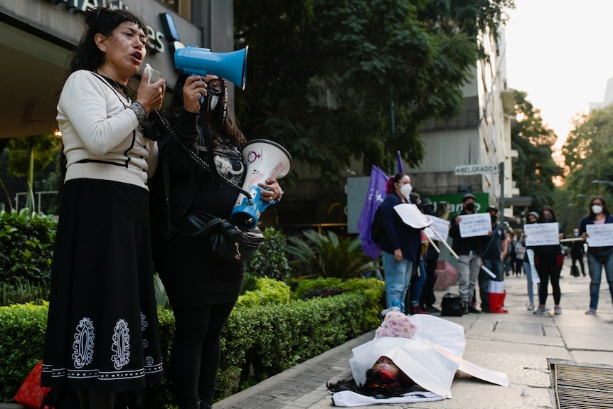 Araceli Osorio with a megaphone at a rally where a woman pretends to lie dead on the floor.