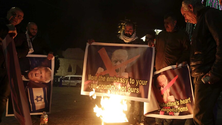 Palestinians stand in the dark burn a poster of the US President Donald Trump