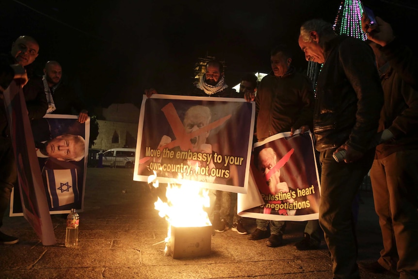 Palestinians stand in the dark burn a poster of the US President Donald Trump