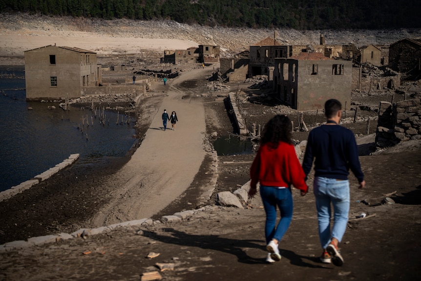 En primer plano, una pareja camina de la mano contra el fondo del pueblo devastado. 