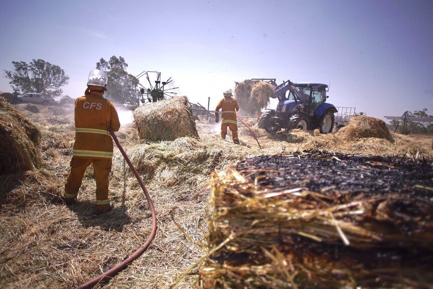 Two Country Fire Service volunteer spray water onto burnt hay bails.