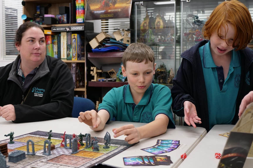 A mother, and her two kids playing a boardgame on one side of a table.