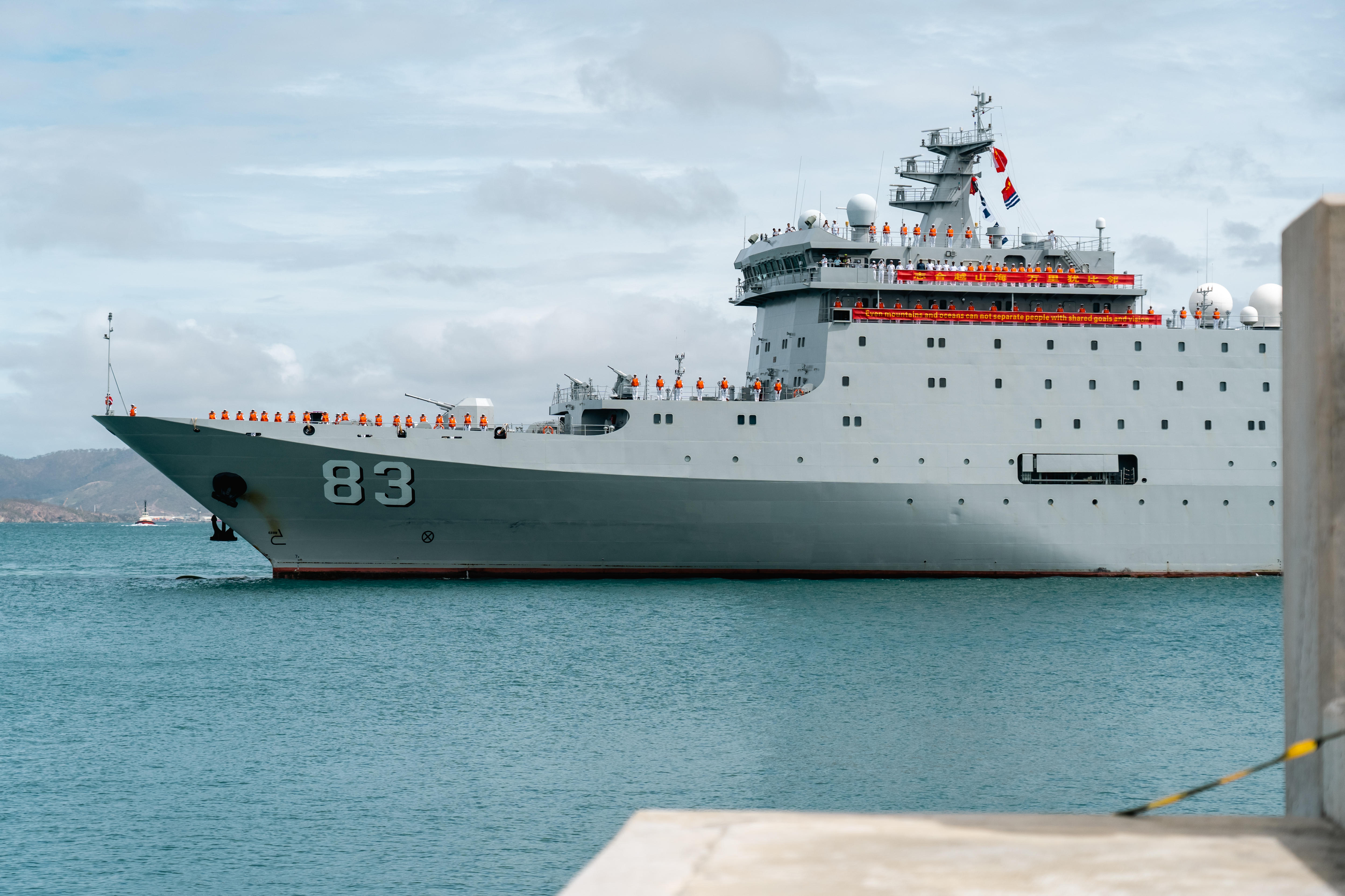 A grey navy vessel in shallow blue waters on an overcast day