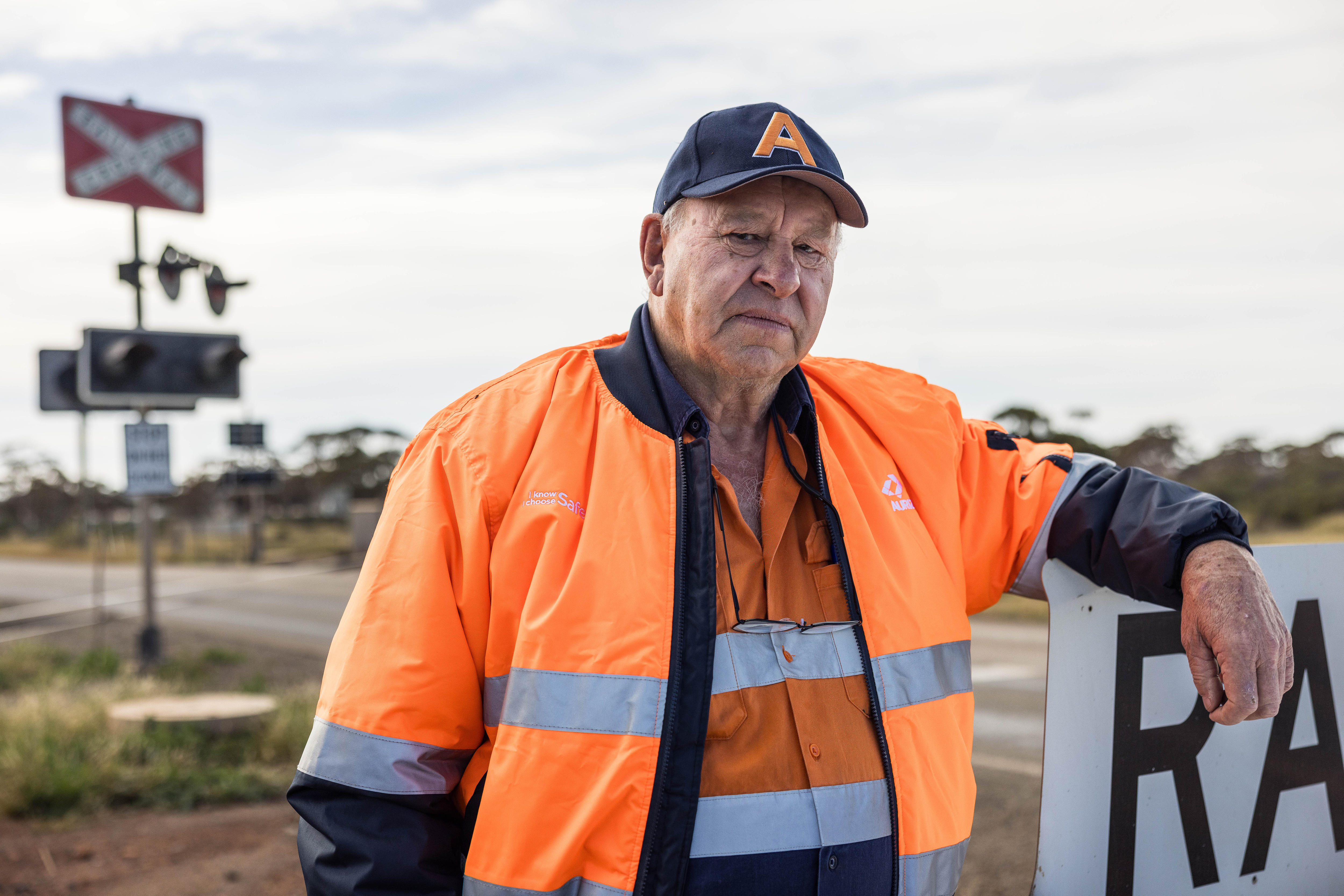 A man wearing high-vis orange workwear leaning on a railway sign.  