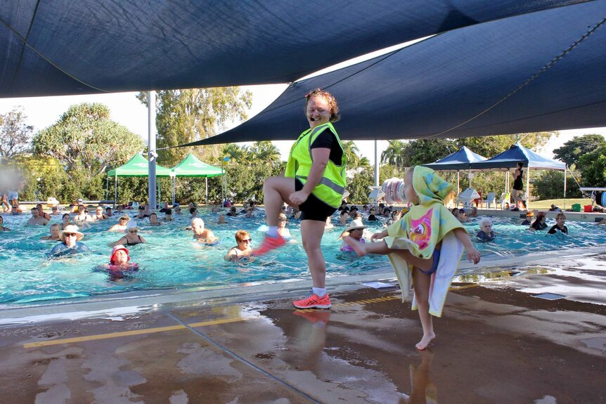 A woman leads an aqua aerobics class with a little girl mimicking her movements alongside
