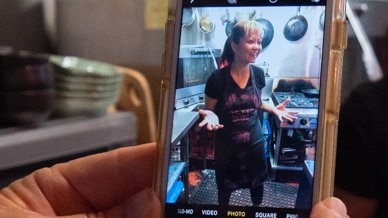 A close up photo on a smart phone of cook Busara O'Reilly stands in her cafe kitchen surrounded by frypans and pots