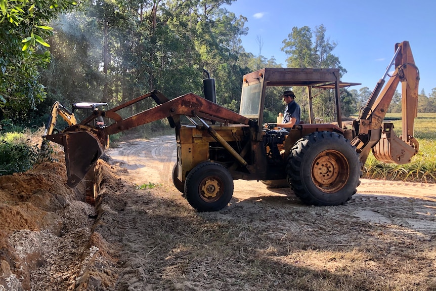 A tractor with a big bucket on the front of it tips woodchips into a trench.