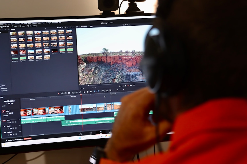 Un hombre con auriculares edita un vídeo en su computadora.