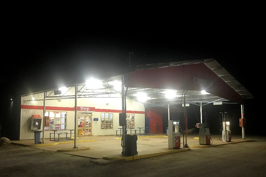 A remote service station with no cars at the bowsers. It's night time and the white lights are bright.