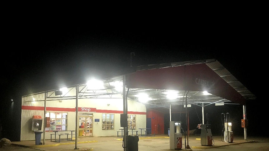 A remote service station with no cars at the bowsers. It's night time and the white lights are bright.