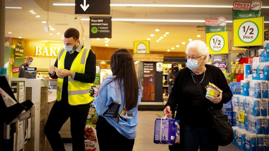 Shoppers wearing face masks near the counter in a Woolworths supermarket, while a worker in a face mask stands near the counter.