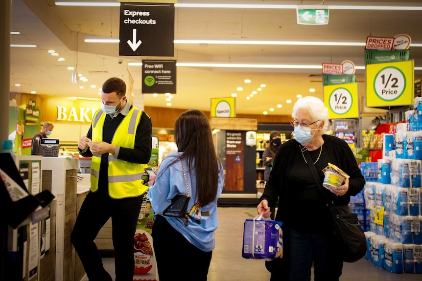 Shoppers wearing face masks near the counter in a Woolworths supermarket, while a worker in a face mask stands near the counter.