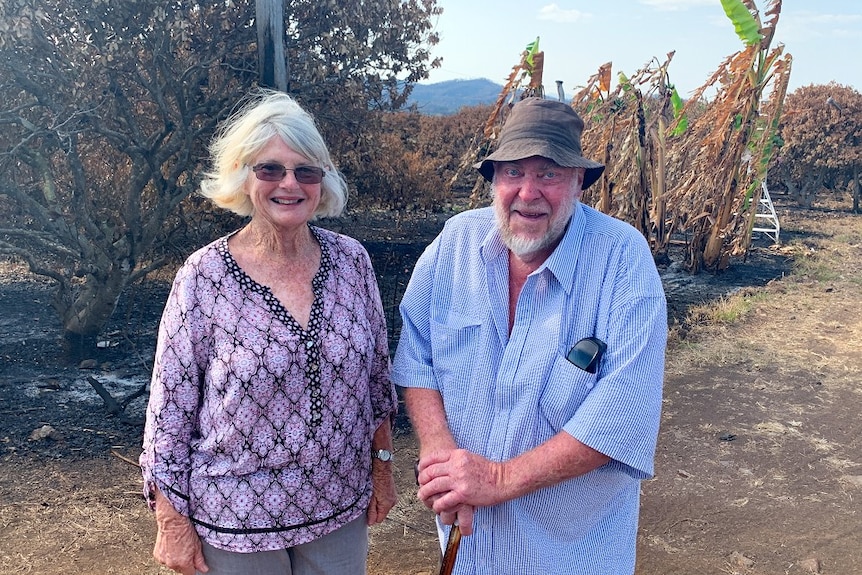 Denise and Tony Welch smile for the camera with their burnt property behind them
