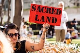 A protestor holds a sign saying 'sacred land' at a Rio Tinto protest.