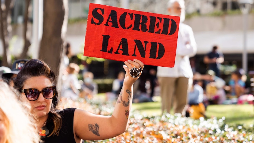 A protester holds a sign saying 'sacred land' at a Rio Tinto protest.