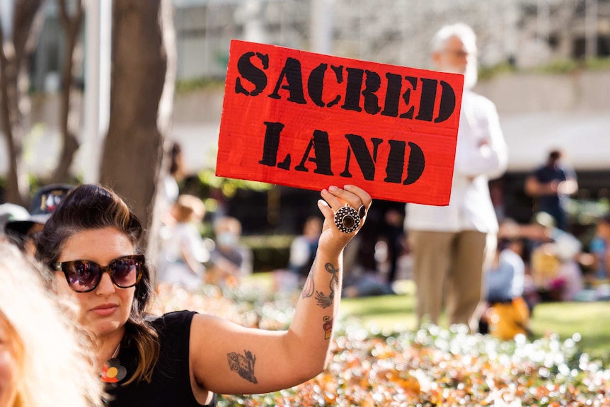 A protester holds a sign saying 'sacred land' at a Rio Tinto protest.