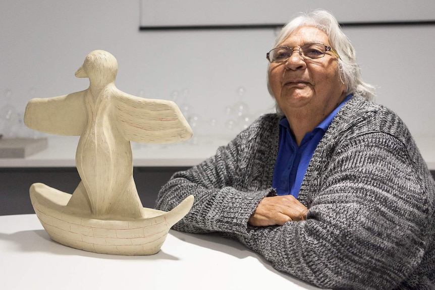 Laurel Nannup sits in front of an upright model bird sculpture.