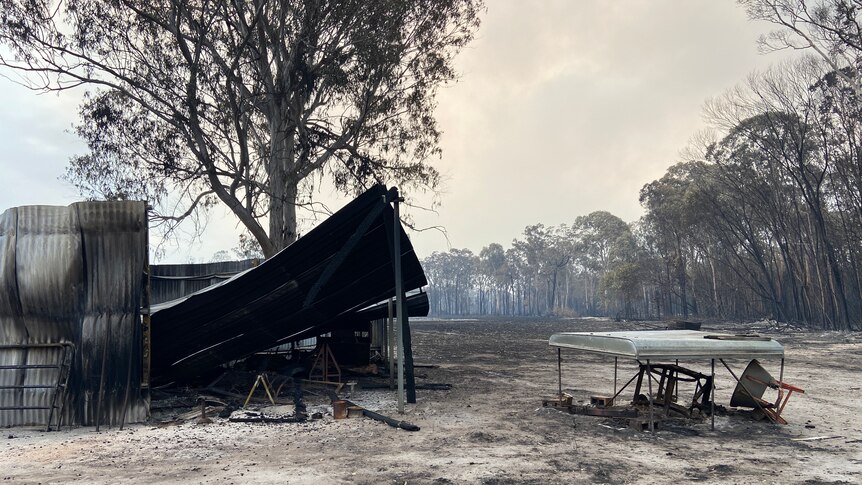 A collapsed shed with metal sheets around, blackened grass, smoke