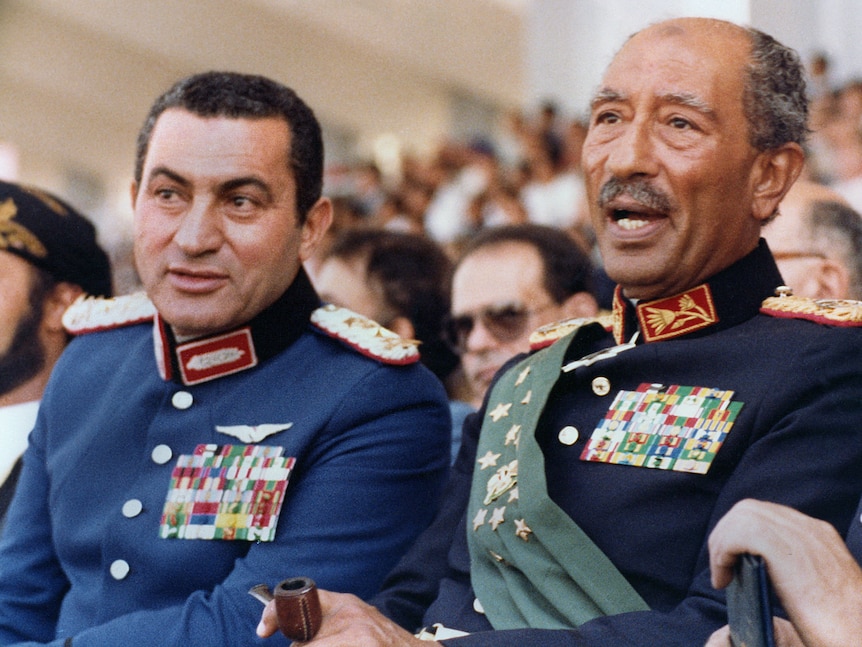 Anwar al-Sadat and Hosni Mubarak sit side by side in military uniforms, decked out with medals
