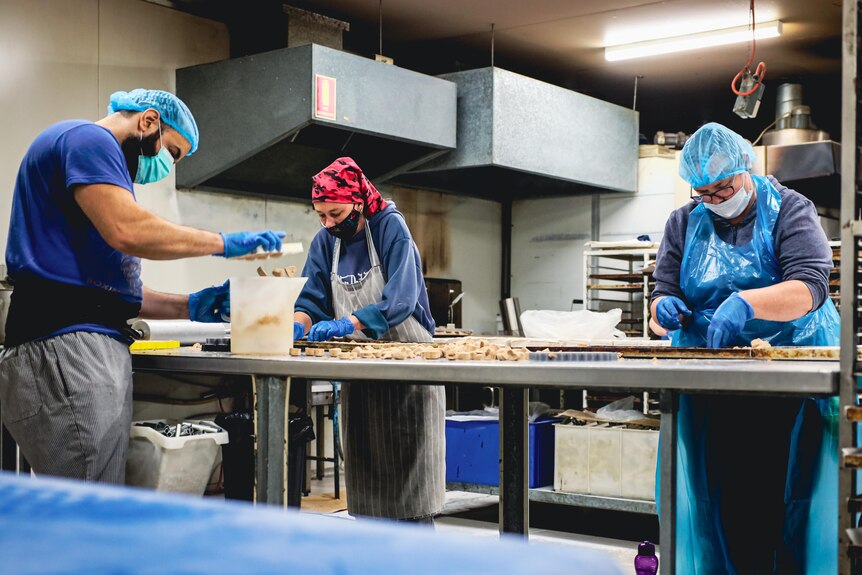 Workers rolling pastry in a commercial kitchen. 