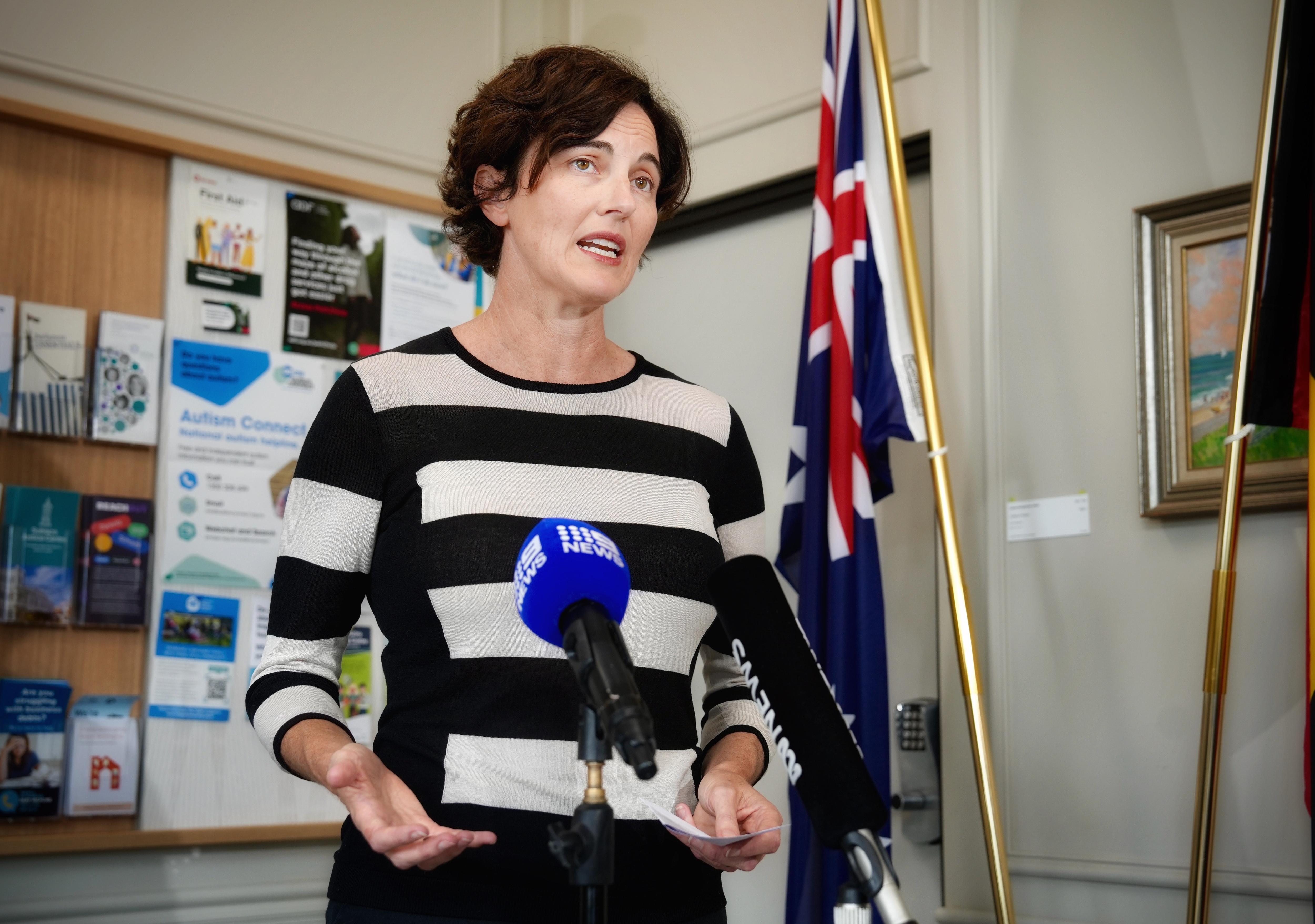 Kate Chaney in a striped shirt speaking to the media and gesturing with her hands.