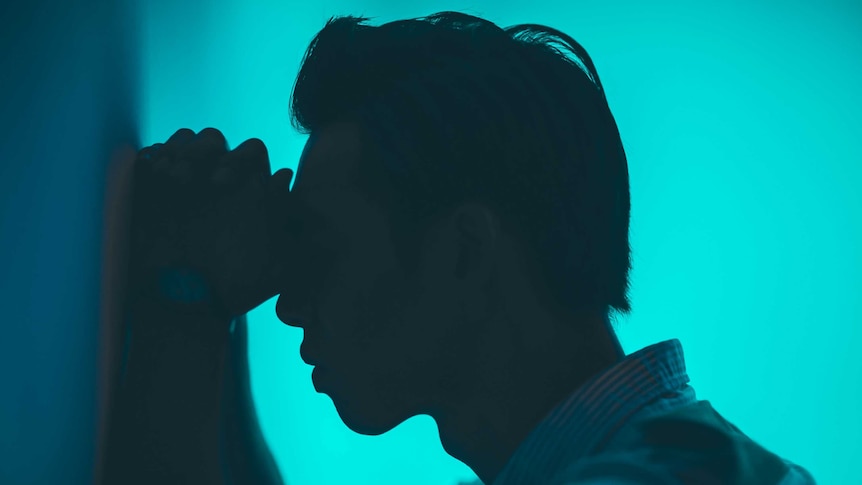 Silhouette of a young man against a blue background, holding his head