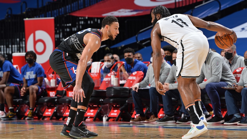 Ben Simmons in a defensive stance as James Harden dribbles a basketball.